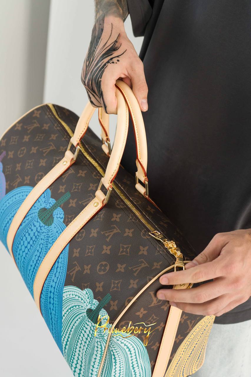 Сумка Сумку Keepall LV YK с плечевым ремнём, созданную для новой эксклюзивной коллекции Louis Vuitton Yayoi Kusama, отличают легендарные красочные тыквы и гипнотические узоры в точку.